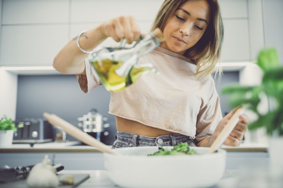 lady in kitchen pouring oil on green salad